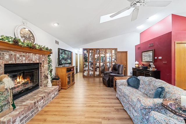 living room featuring lofted ceiling, a brick fireplace, light hardwood / wood-style flooring, and ceiling fan