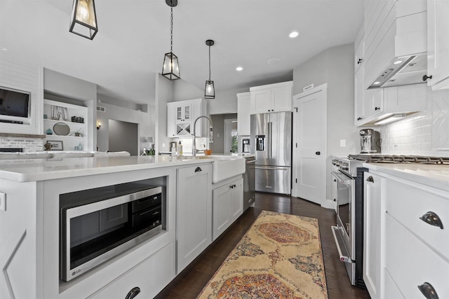 kitchen featuring pendant lighting, wall chimney range hood, white cabinetry, stainless steel appliances, and an island with sink