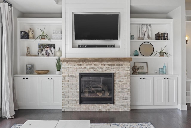 living room with a brick fireplace, built in features, and dark hardwood / wood-style flooring