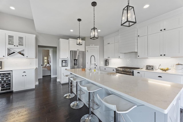 kitchen with premium appliances, a kitchen island with sink, hanging light fixtures, and white cabinets