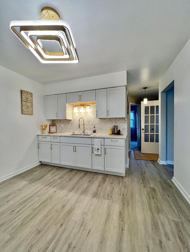 kitchen featuring tasteful backsplash, decorative light fixtures, sink, and light hardwood / wood-style flooring