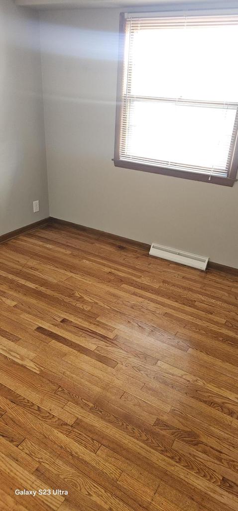 empty room featuring wood-type flooring and baseboard heating