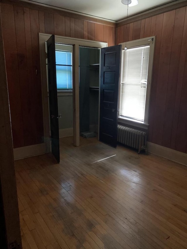 unfurnished bedroom featuring hardwood / wood-style flooring, radiator heating unit, and wooden walls