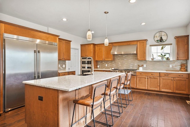 1452 Serenity Ct, Sun Prairie, WI 53590 - kitchen featuring wall chimney range hood, stainless steel appliances, brown cabinets, and dark wood-type flooring