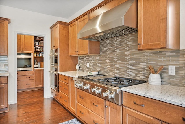 1452 Serenity Ct, Sun Prairie, WI 53590 - kitchen with brown cabinetry, wall chimney range hood, light stone counters, dark wood finished floors, and stainless steel appliances