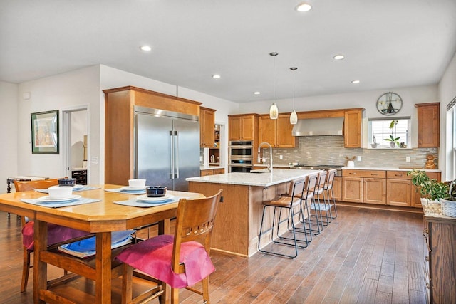 1452 Serenity Ct, Sun Prairie, WI 53590 - kitchen with dark wood-style floors, wall chimney range hood, a center island with sink, recessed lighting, and appliances with stainless steel finishes