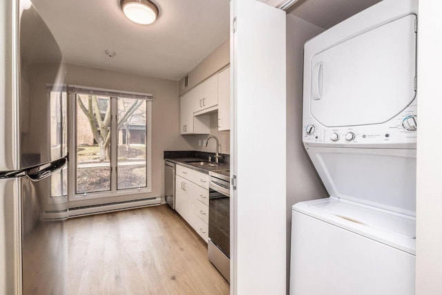 washroom featuring a baseboard radiator, light wood-style flooring, a sink, stacked washing maching and dryer, and laundry area