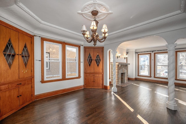 foyer entrance featuring crown molding, dark wood-type flooring, decorative columns, a notable chandelier, and a brick fireplace