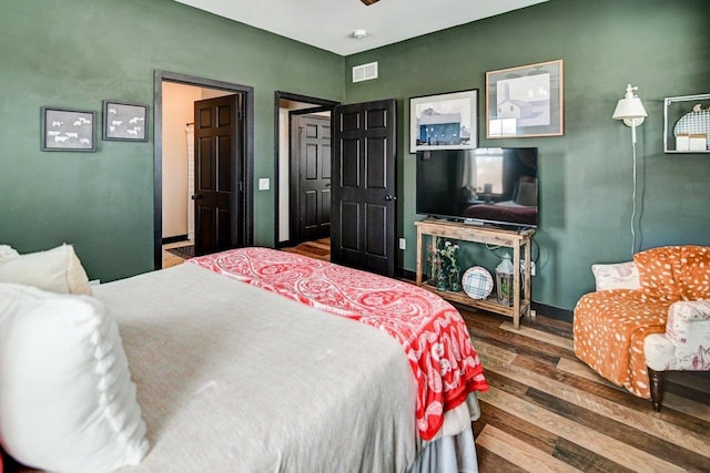 bedroom with a ceiling fan, visible vents, baseboards, and wood finished floors