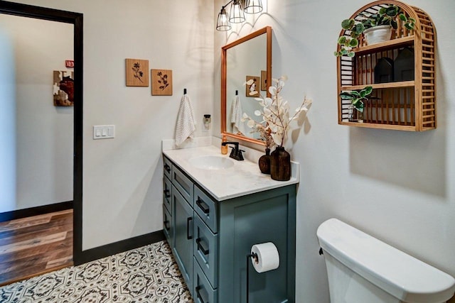 half bathroom featuring toilet, wood finished floors, vanity, and baseboards