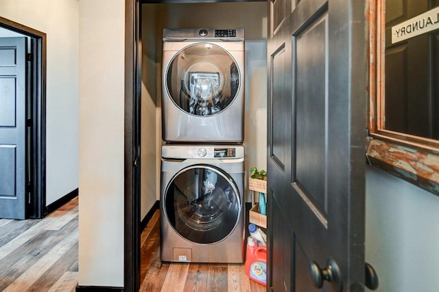 clothes washing area with baseboards, stacked washer / drying machine, and wood finished floors