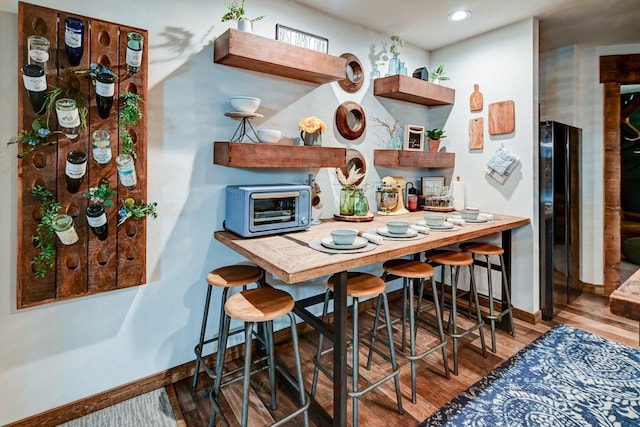 kitchen featuring a toaster, open shelves, freestanding refrigerator, wood finished floors, and baseboards