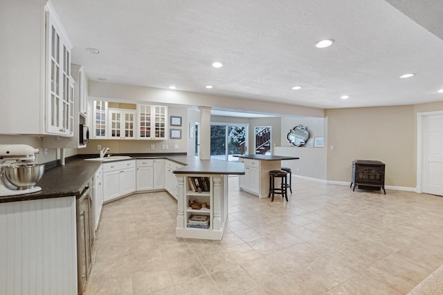 kitchen with a breakfast bar, sink, a textured ceiling, a kitchen island, and white cabinets