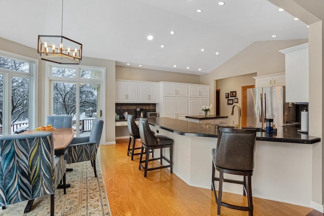 kitchen with a kitchen bar, light hardwood / wood-style flooring, stainless steel refrigerator, pendant lighting, and white cabinets