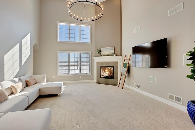 living room with light colored carpet, a tile fireplace, a chandelier, and a high ceiling