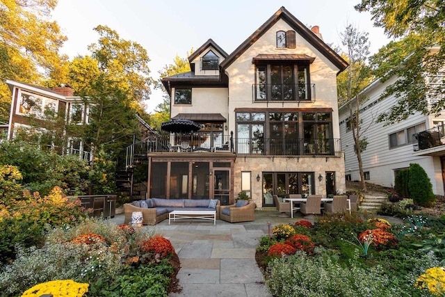 rear view of house with a balcony, a standing seam roof, stucco siding, a patio area, and an outdoor hangout area