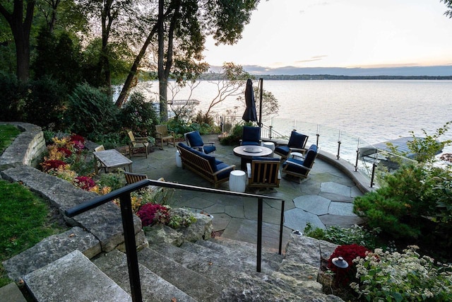 patio terrace at dusk featuring an outdoor fire pit, a dock, and a water view