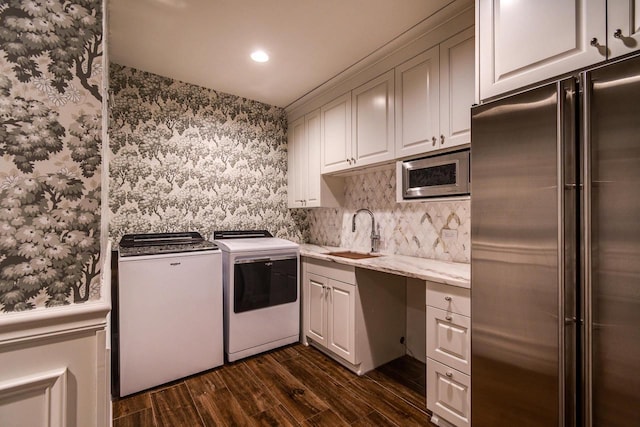 laundry area featuring a sink, wallpapered walls, separate washer and dryer, cabinet space, and dark wood-style flooring