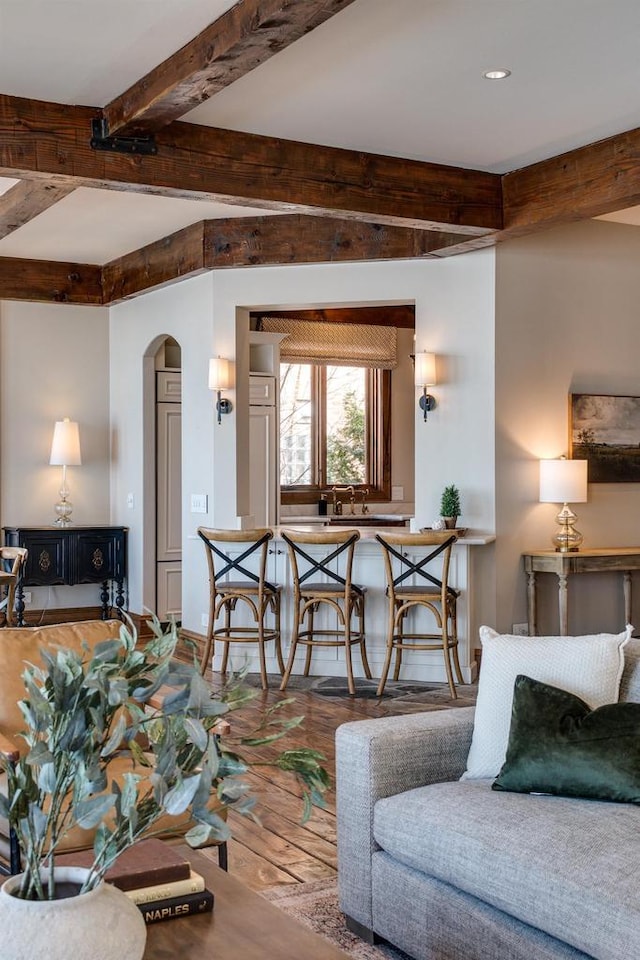 living area with arched walkways, beamed ceiling, and wood finished floors