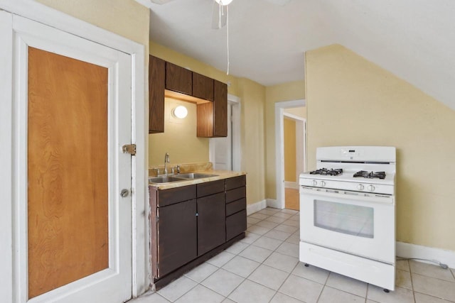 kitchen with white gas range oven, sink, dark brown cabinets, ceiling fan, and light tile patterned floors