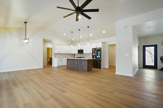 kitchen featuring light hardwood / wood-style flooring, hanging light fixtures, stainless steel fridge, a kitchen island with sink, and white cabinets