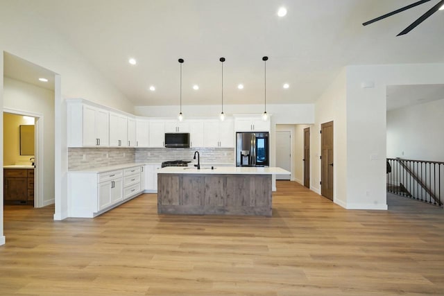 kitchen with stainless steel refrigerator with ice dispenser, light wood-type flooring, pendant lighting, a kitchen island with sink, and white cabinets