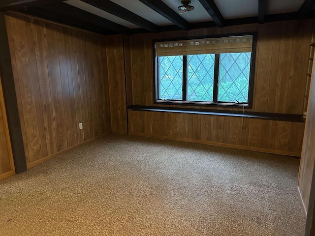 carpeted spare room with beam ceiling and wood walls