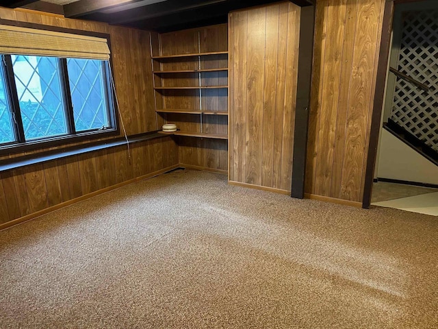 carpeted spare room featuring beam ceiling and wooden walls