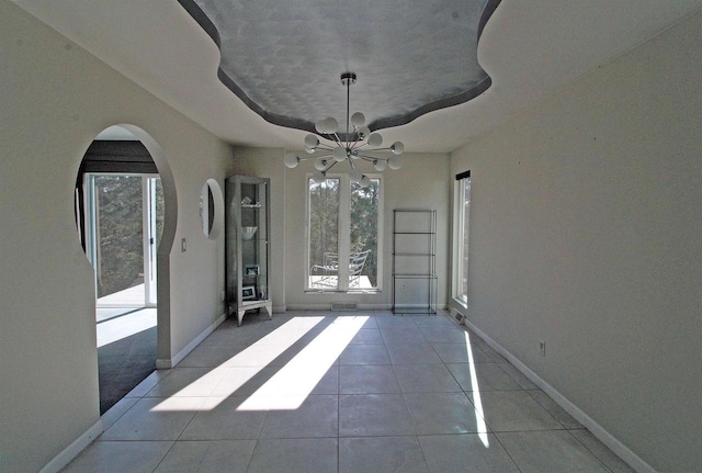 unfurnished dining area with an inviting chandelier, baseboards, arched walkways, and tile patterned floors