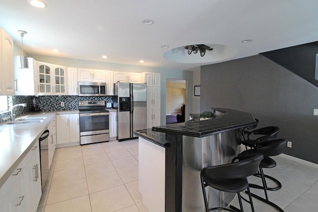 kitchen featuring glass insert cabinets, a breakfast bar, decorative backsplash, stainless steel appliances, and a sink