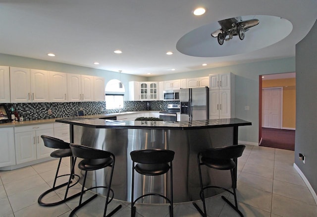 kitchen with light tile patterned floors, glass insert cabinets, a kitchen breakfast bar, and appliances with stainless steel finishes