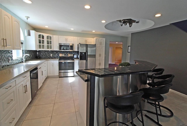 kitchen with decorative backsplash, stainless steel appliances, a breakfast bar area, light tile patterned floors, and glass insert cabinets