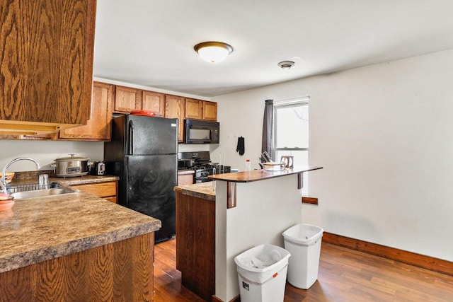 kitchen with sink, dark wood-type flooring, black appliances, and a kitchen breakfast bar