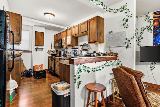 kitchen featuring dark wood-type flooring, black appliances, and a breakfast bar