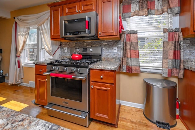 kitchen with tasteful backsplash, appliances with stainless steel finishes, stone countertops, and light hardwood / wood-style flooring