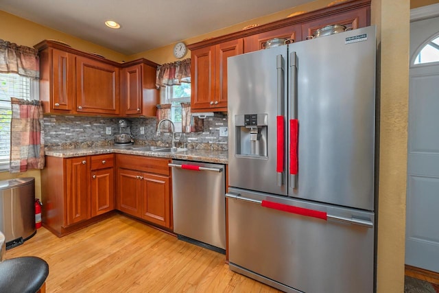 kitchen with light stone counters, appliances with stainless steel finishes, sink, and light hardwood / wood-style flooring