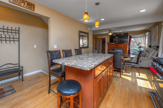 kitchen featuring a breakfast bar, a fireplace, hanging light fixtures, a center island, and light hardwood / wood-style flooring