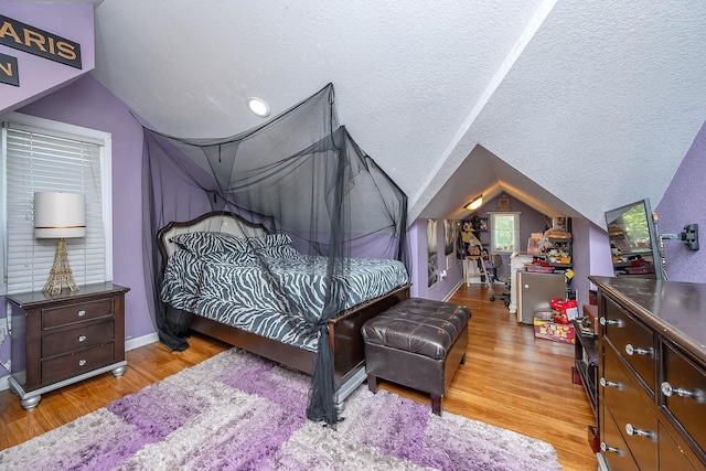 bedroom with lofted ceiling, light hardwood / wood-style floors, and a textured ceiling