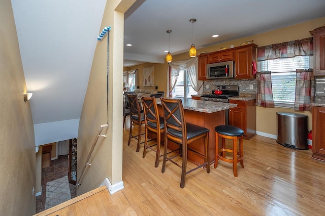 kitchen with a breakfast bar, tasteful backsplash, hanging light fixtures, stove, and light hardwood / wood-style floors