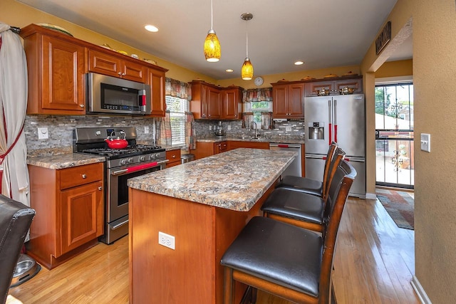 kitchen featuring appliances with stainless steel finishes, pendant lighting, a breakfast bar area, a center island, and light stone countertops