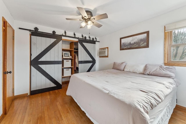 bedroom featuring ceiling fan, wood-type flooring, a barn door, and a wall unit AC