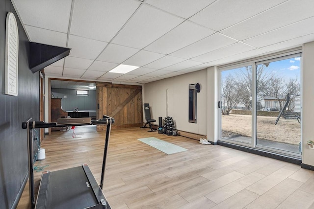 workout room featuring wooden walls, a drop ceiling, and light wood-type flooring