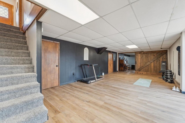 workout room with light hardwood / wood-style flooring, wood walls, and a paneled ceiling