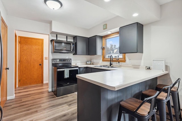 kitchen featuring sink, a breakfast bar area, appliances with stainless steel finishes, kitchen peninsula, and light hardwood / wood-style floors