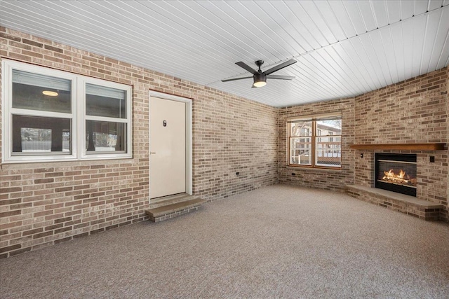 unfurnished living room with carpet, ceiling fan, a brick fireplace, and brick wall