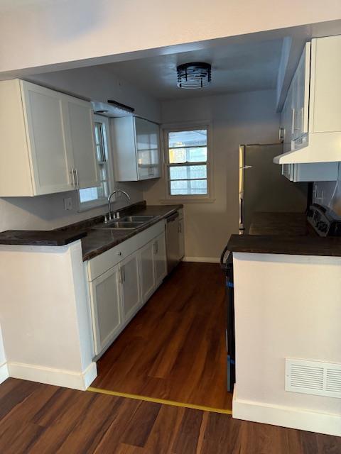 kitchen with dark wood-type flooring, stainless steel dishwasher, sink, and white cabinets