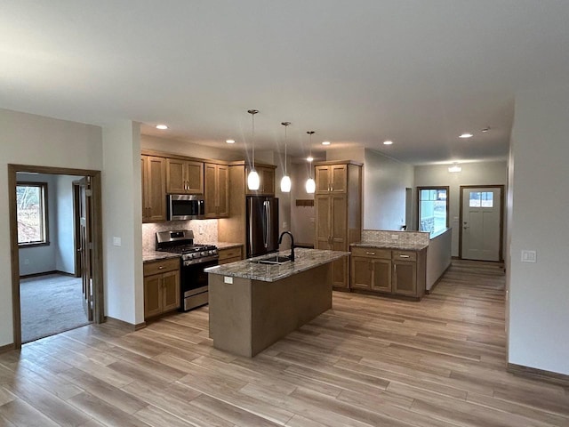 kitchen with hanging light fixtures, light stone countertops, appliances with stainless steel finishes, and a kitchen island with sink