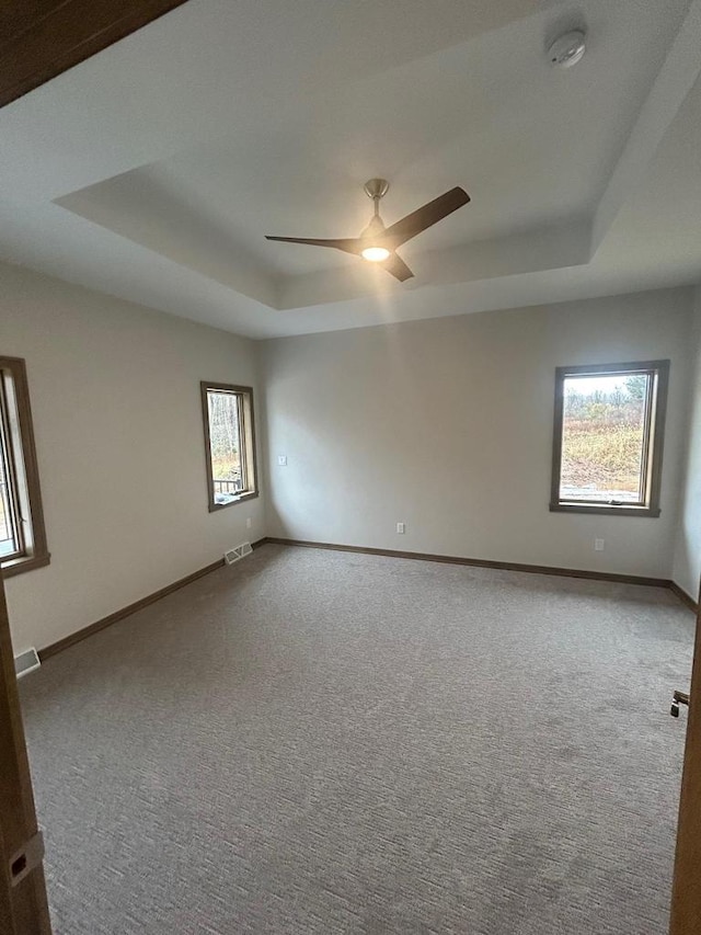 unfurnished room with ceiling fan, a tray ceiling, and carpet