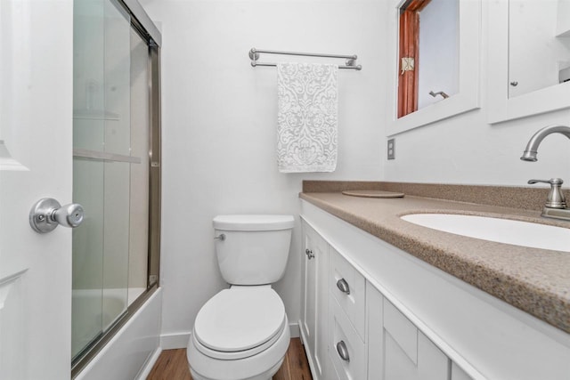 full bathroom featuring hardwood / wood-style flooring, vanity, shower / bath combination with glass door, and toilet