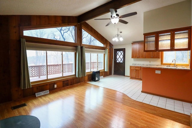 kitchen with sink, vaulted ceiling with beams, wood walls, and light hardwood / wood-style flooring